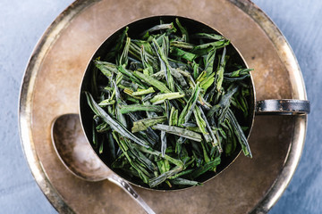 Dry green tea leaves in wooden spoon over brown plate