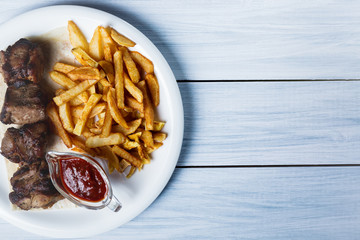 Grilled shish kebab served with french fries and sauce on blue wooden table