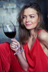 Elated Caucasian girl with a glass of red wine looking sideward