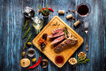 Sliced medium rare t-bone steak on rustic wooden background with rosemary and spices