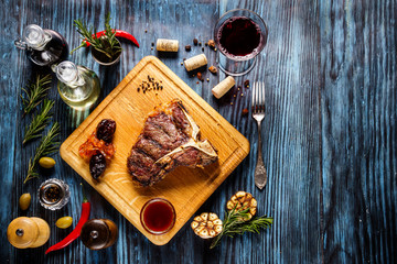 Medium rare grilled t-bone steak on rustic wooden background with rosemary and spices