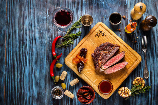 Sliced medium rare grilled steak on rustic wooden background with rosemary and spices