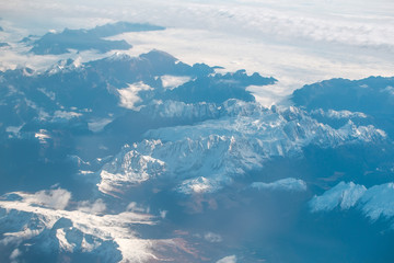 Fototapeta na wymiar Idyllic snowy mountain peaks under clouds from plane