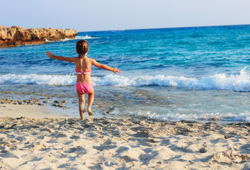 Happy  Cute Little Girl running  on the coast of warm Sea at Summer Sunset