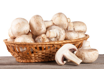 Champignon mushrooms in a wicker basket on a wooden table with white background