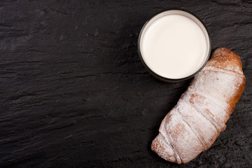 glass of milk with croissants on black stone background with copy space for your text. Top view