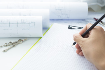 Architecture, engineering and construction background concept. Drawings for building Architectural project.Hand holding drawing pencil,blueprint rolls,dividers and clipboard  on desk.Selective focus.