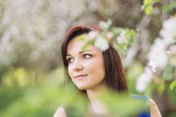 Naklejka premium beautiful young brunette woman standing near the blossoming apple tree on a warm spring day