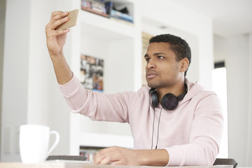 Take a selfie. Cropped shot of a handsome Afro American young man using his cellphone and taking selfie while chilling at home.