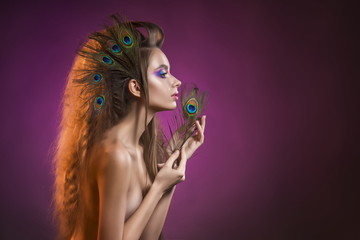 portrait of the young girl with a vanguard hairstyle and feathers of a peacock on a violet...