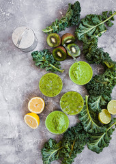 Fototapeta na wymiar Greenery group smoothie glasses. Fresh green smoothie in glasses with kale leaves, kiwi fruit and lime in tray. Clean eating, detox and healthy food concept. Top view.