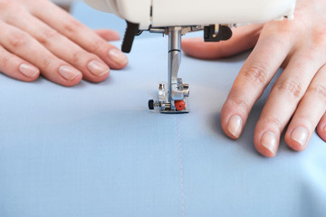 Seamstress threading blue textile on sewing machine close up