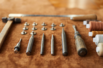 Artisan tools for working with leather: hammer, scissors, thick thread, metal wire, awl, buttons on leather background