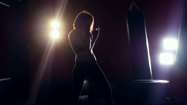 Female boxer training. Woman silhouette making shadowboxing. Strong light behind her. 4K.