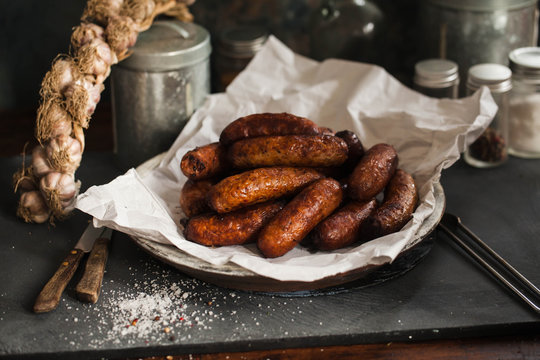 Bunch OF Fried Sausages on Plate Over White Paper WIth Garlic Braid And Spcies' Containers