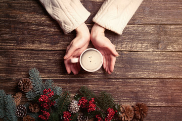 female hands holding cup of coffee near christmas decorations on the brown wooden background