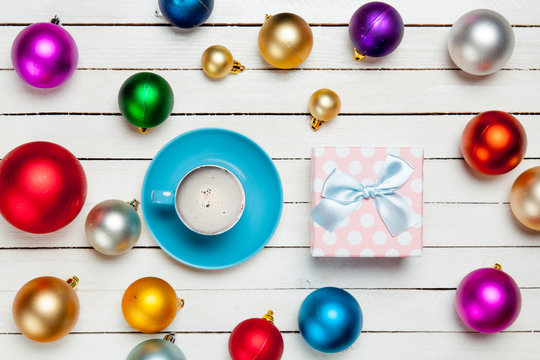 photo of blue cup of coffee and cute gift near colorful baubles on the wonderful white wooden background