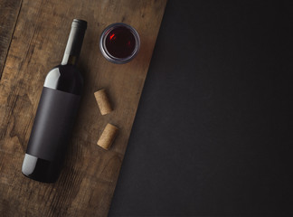 Bottle of red wine with label on old board. Glass of wine and cork. Wine bottle mockup. Top view. - obrazy, fototapety, plakaty