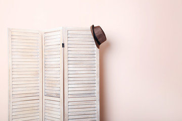 Hat hanging on wooden folding screen on a beige background