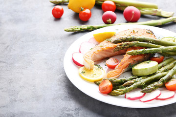 Steak of salmon with asparagus and vegetables on grey wooden table