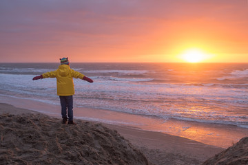 Child observing sunset on a winter beach in Texel, the Netherlands.