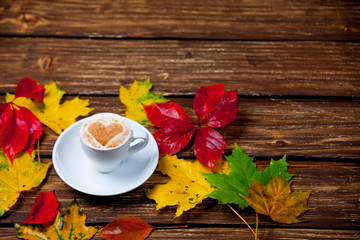 photo of cup of coffee and autumn leaves on the wonderful brown wooden background