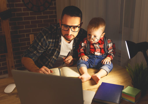 father and son baby work at home at computer in dark .