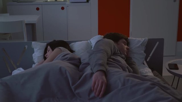 Young family sleeping in bed. Girlfriend and boyfriend wearing in sleepwear rest in flat. Woman and man lying on the white pillow covered with a grey blanket.