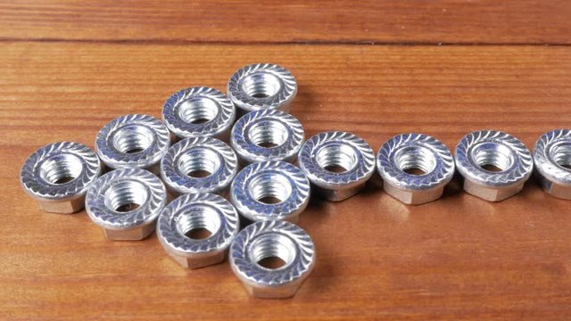Nuts for bolts lie on a wooden table in the form of an arrow. Moving on the slider camera.