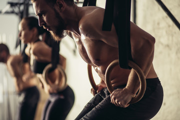 tree attractive young male and female adults doing pull ups on bar in cross fit training gym with brick walls and black mats