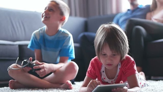 brother palying video games while sister using tablet in living room