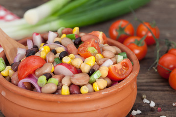 Vegetarian salad with red and black beans, chickpeas and corn in clay bowl