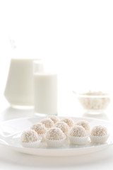 Raffaello candy in baskets on a plate, with milk in a glass and jug, cottage cheese in a bowl in the background, on a white table, in a high key, with space for text