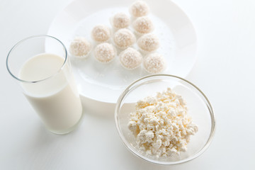 Raffaello candy in baskets on a plate, with milk in a glass and jug, cottage cheese in a bowl in the background, on a white table, in a high key, with space for text