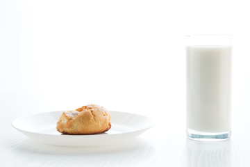 Milk in a glass, an eclair cake in a plate, on a white table, in a high key, with space for text