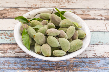 Fresh green unripe almonds on white plate in vintage table