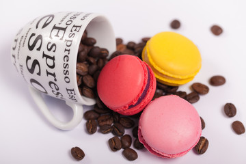 Cup with coffee beans with colorful delicious French macaroons on white background close up
