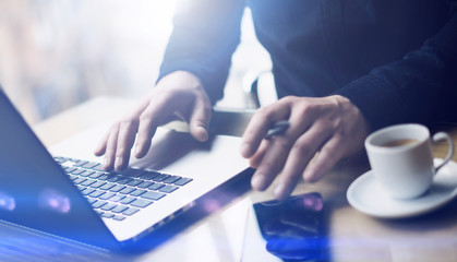 Man working at the wooden table at modern loft office.Man sitting at workplace and typing on laptop keyboard.Blurred background.Horizontal,visual effects.