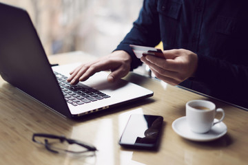 Businessman holding plastic credit card in hand and using laptop computer while sitting at the...