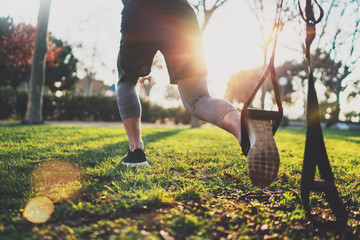 Healthy lifestyle concept.Muscular athlete exercising trx outside in sunny park.Great TRX workout.Young handsome man in sportswear doing exercising outdoors.Blurred background,flare.