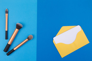 Make up brushes with yellow envelope and blank card on blue background