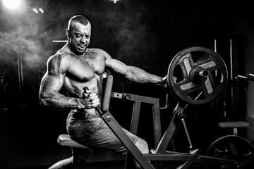 Fototapeta na wymiar Strong Bodybuilder Doing Heavy Weight Exercise For Back On Machine. Smoke on background