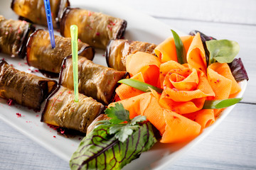 Egg-plant roll with cheese and nice rose like carrot on white plate with selective focus