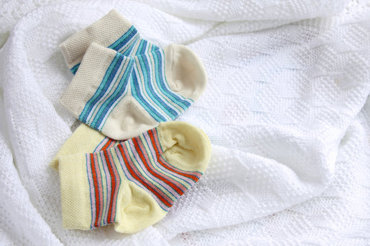 two pairs of baby socks: blue and yellow striped on crocheted blanket, white background with copy space