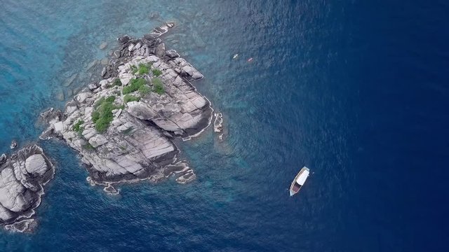Aerial top view shot of a rocky tropical island and a scuba diving boat next to it. Snorkelers, divers, and kayakers on clear blue waters.
