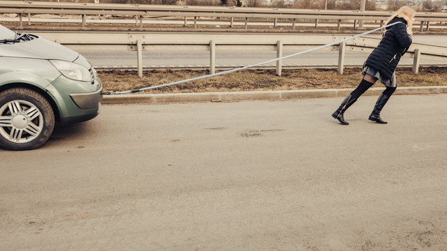 Woman pulling broken car on road