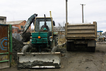 Fototapeta na wymiar An old Soviet tractor digs and loads waste stone processing near the shop