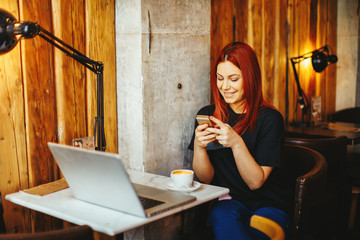 Young woman texting on the phone with a laptop on table in cafe