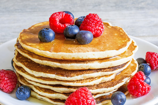 pile of homemade pancakes with fresh berries and honey
