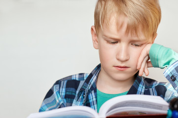 Book, school, kid. Little schoolboy with blond hair dressed in checked shirt siting and looking...